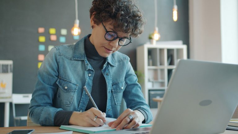 Online course assessment: learner taking notes next to her laptop